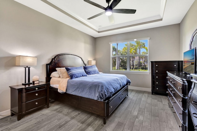 bedroom with a raised ceiling, ceiling fan, and light hardwood / wood-style flooring