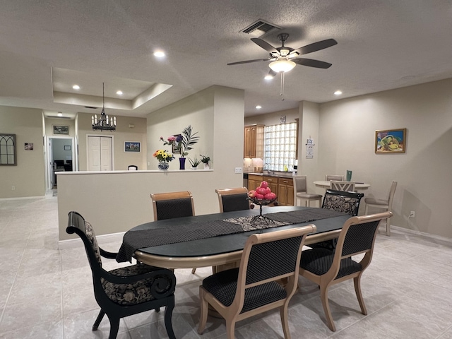 dining room with light tile patterned flooring, ceiling fan with notable chandelier, a textured ceiling, and a tray ceiling