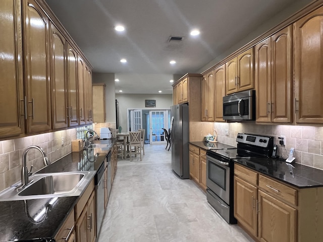 kitchen featuring stainless steel appliances, sink, decorative backsplash, and dark stone countertops