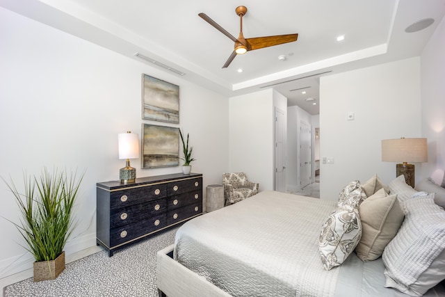 carpeted bedroom with ceiling fan and a tray ceiling