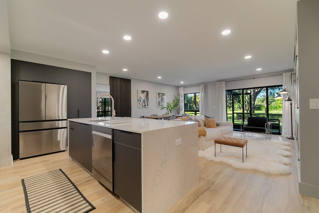 kitchen with a kitchen island with sink, sink, light hardwood / wood-style floors, and appliances with stainless steel finishes