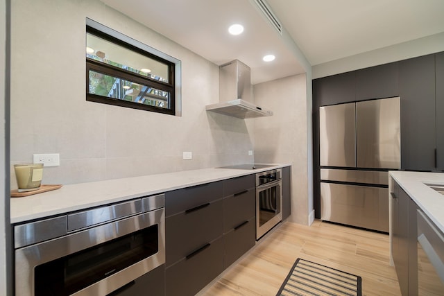 kitchen with stainless steel appliances, light hardwood / wood-style floors, and wall chimney range hood