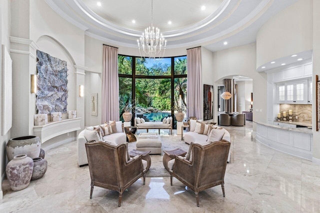 living room with arched walkways, a high ceiling, a tray ceiling, crown molding, and a chandelier