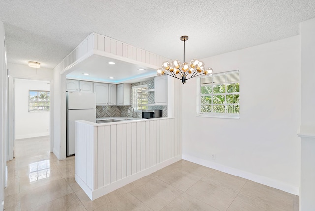 148 Yacht Club Dr Unit 12, North Palm Beach, FL 33408 - kitchen featuring stainless steel microwave, freestanding refrigerator, backsplash, a peninsula, and a chandelier