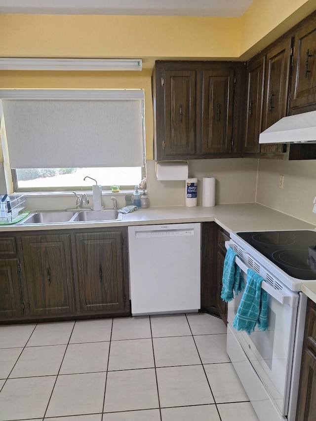 kitchen featuring dark brown cabinetry, under cabinet range hood, white appliances, a sink, and light countertops