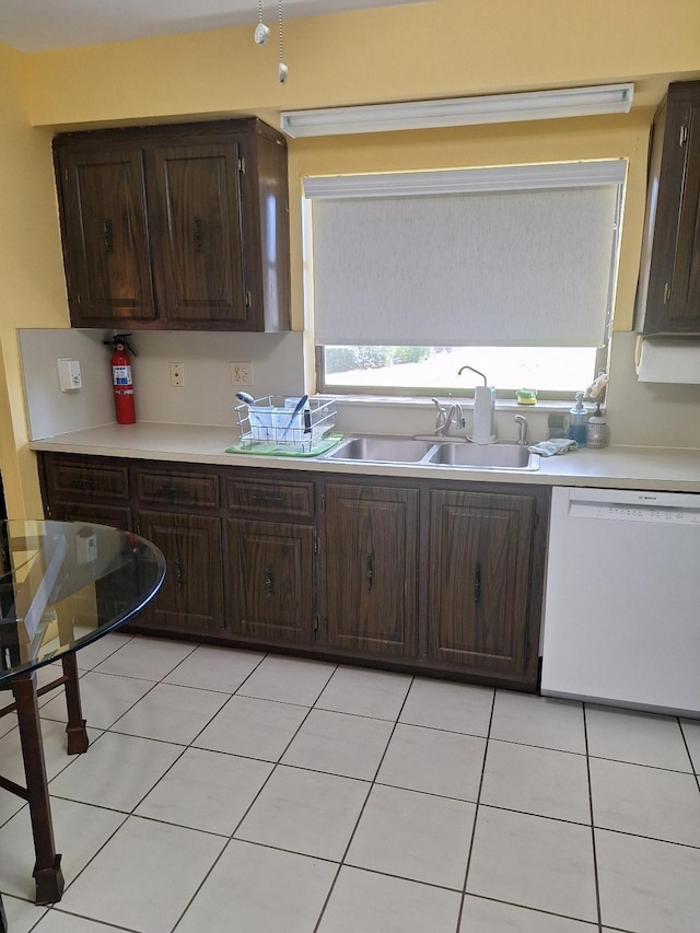 kitchen with light tile patterned floors, dark brown cabinetry, a sink, light countertops, and dishwasher