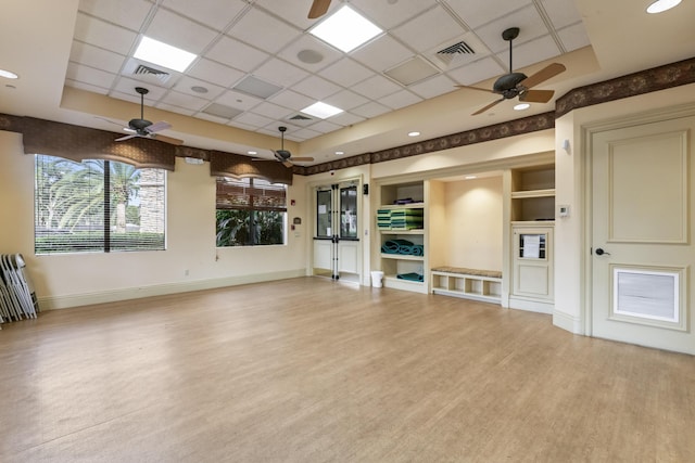 unfurnished living room featuring built in shelves, a paneled ceiling, light hardwood / wood-style flooring, a raised ceiling, and ceiling fan