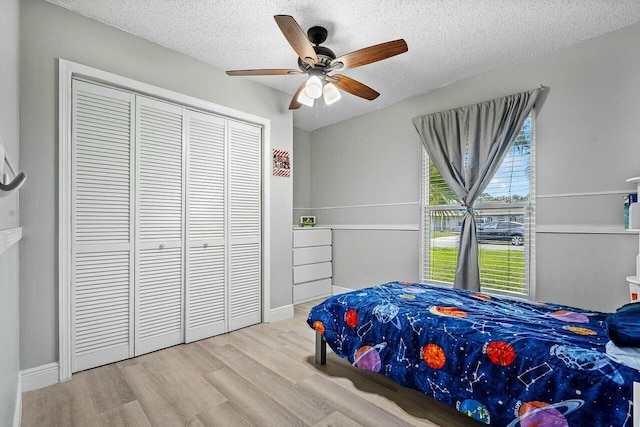 bedroom with ceiling fan, a closet, light hardwood / wood-style floors, and a textured ceiling