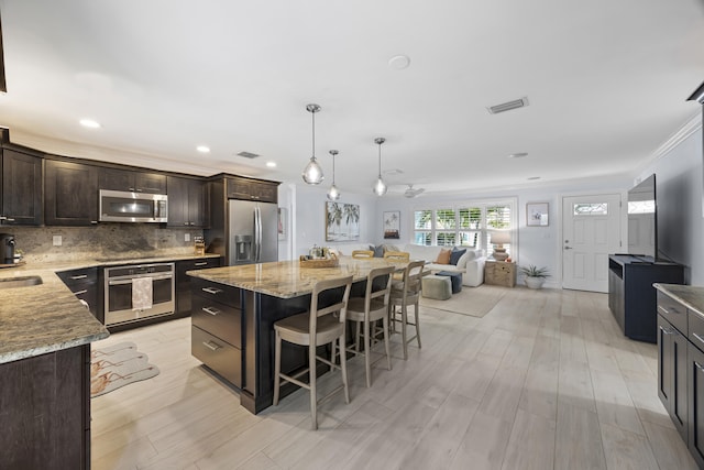 kitchen featuring a breakfast bar, appliances with stainless steel finishes, hanging light fixtures, backsplash, and a center island