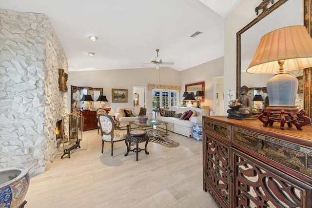 living room featuring ceiling fan, lofted ceiling, a stone fireplace, and light wood-type flooring