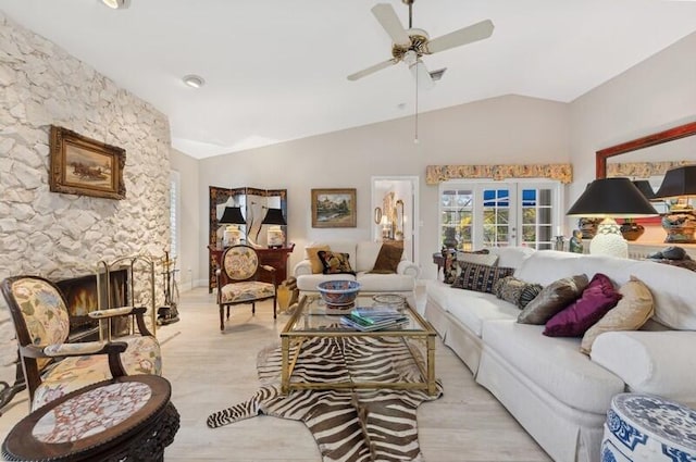 living room featuring french doors, a stone fireplace, vaulted ceiling, ceiling fan, and light hardwood / wood-style floors