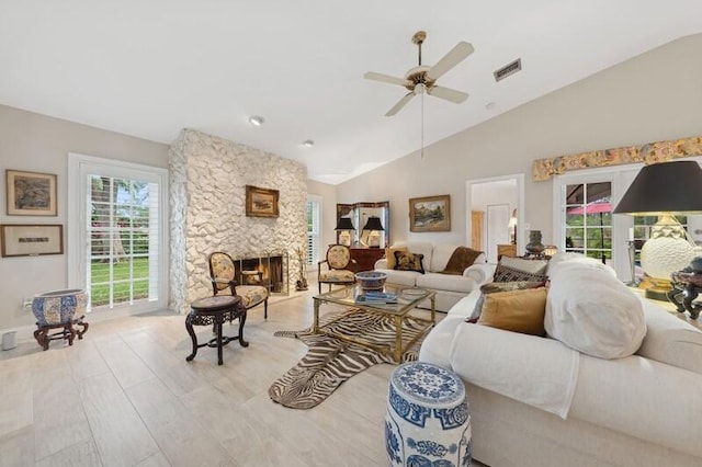 living room featuring ceiling fan, a stone fireplace, and vaulted ceiling