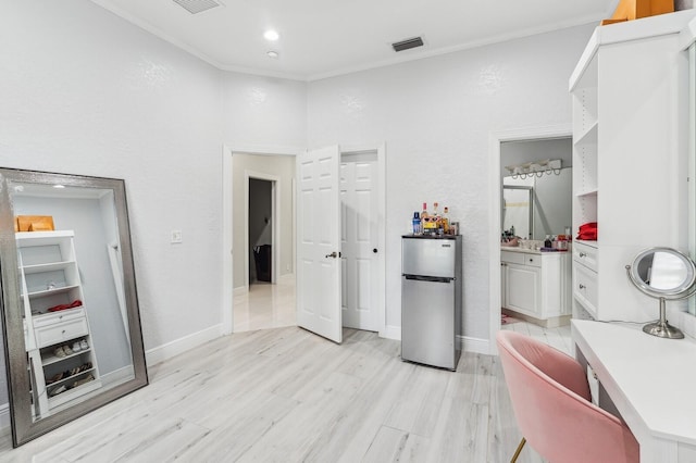 bedroom featuring connected bathroom, light wood-type flooring, crown molding, and stainless steel fridge