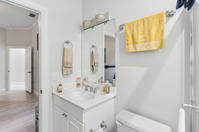 bathroom with hardwood / wood-style flooring, toilet, ornamental molding, a textured ceiling, and vanity