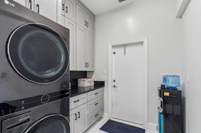 clothes washing area with cabinets, light tile patterned floors, and stacked washing maching and dryer