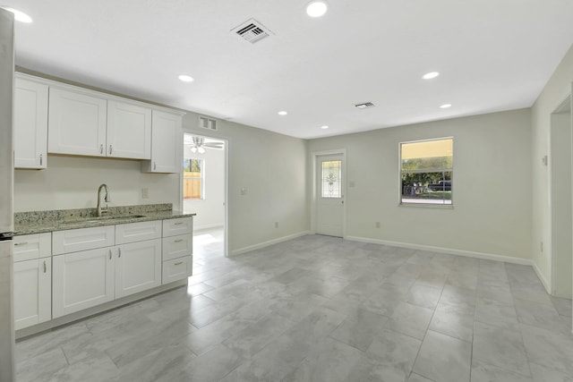 kitchen featuring a healthy amount of sunlight, sink, light stone countertops, and white cabinets