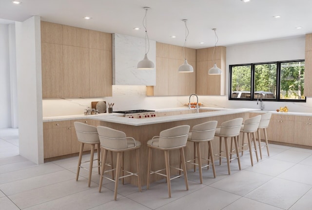 kitchen with a kitchen bar, white gas cooktop, an island with sink, and light brown cabinets