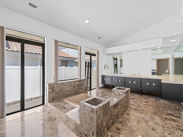 bathroom featuring vanity, vaulted ceiling, and tiled tub