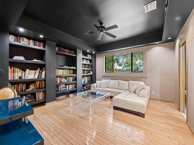 living area featuring ceiling fan, built in features, light wood-type flooring, and a tray ceiling