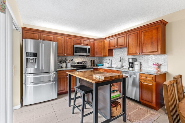 kitchen with light tile patterned flooring, sink, appliances with stainless steel finishes, light stone countertops, and decorative backsplash