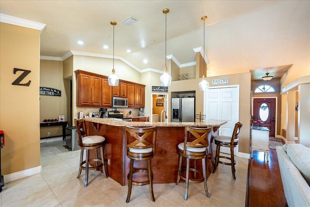 kitchen featuring hanging light fixtures, appliances with stainless steel finishes, a kitchen breakfast bar, an island with sink, and light stone countertops