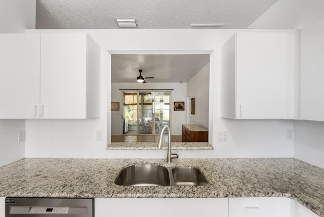 kitchen featuring sink, backsplash, white cabinets, stainless steel dishwasher, and light stone counters