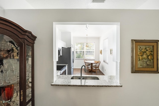 kitchen with stainless steel appliances, sink, pendant lighting, and light stone counters