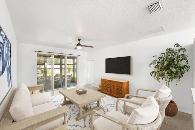 living room with ceiling fan, a textured ceiling, visible vents, and attic access