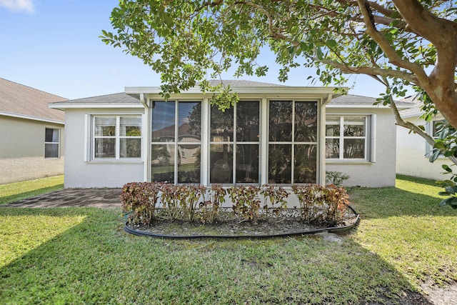 back of property with a yard, a sunroom, and stucco siding