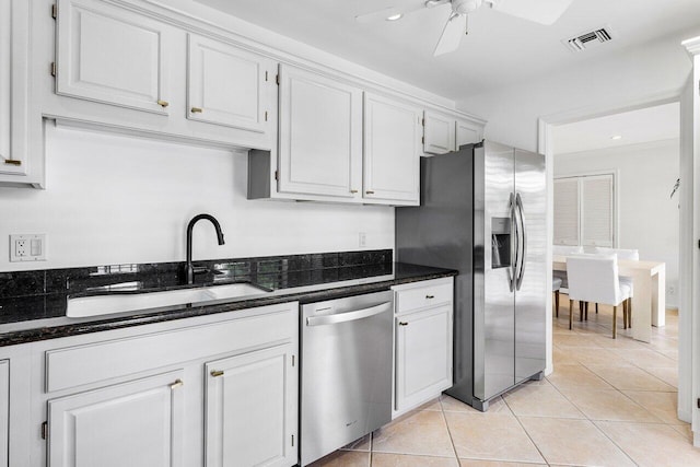 kitchen with sink, light tile patterned floors, stainless steel appliances, white cabinets, and dark stone counters