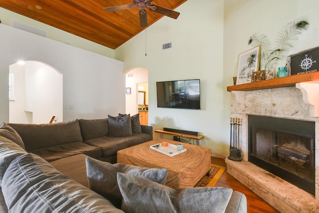 living room with visible vents, arched walkways, a fireplace with raised hearth, wood ceiling, and wood finished floors