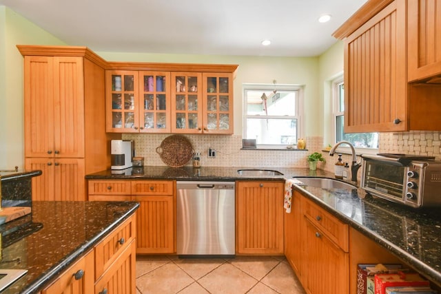 kitchen featuring light tile patterned floors, glass insert cabinets, backsplash, stainless steel dishwasher, and a sink