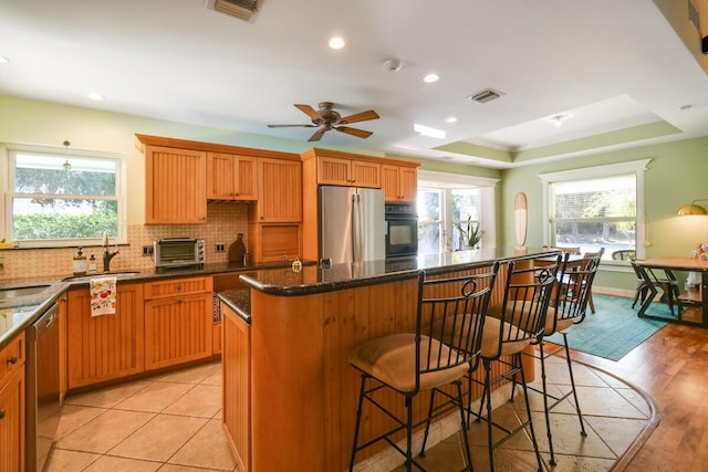 kitchen with visible vents, a kitchen island, appliances with stainless steel finishes, a tray ceiling, and a sink