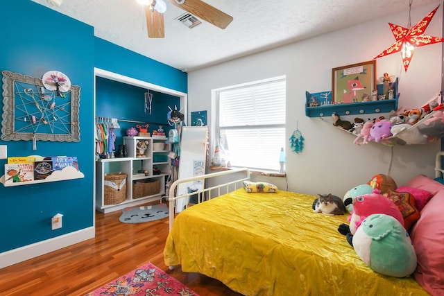 bedroom featuring a textured ceiling, wood finished floors, visible vents, baseboards, and a ceiling fan