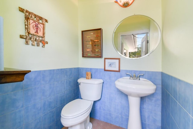 half bath with wainscoting, toilet, and tile walls