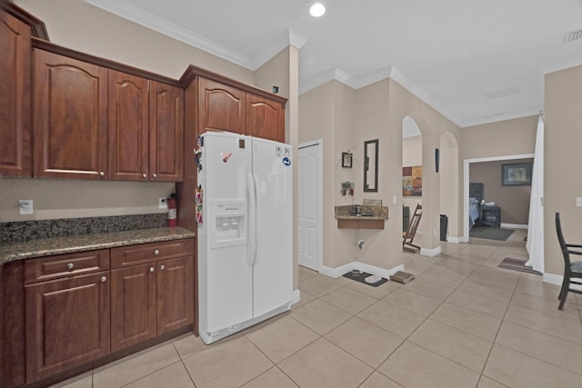 kitchen featuring dark stone countertops, light tile patterned floors, white refrigerator with ice dispenser, and ornamental molding