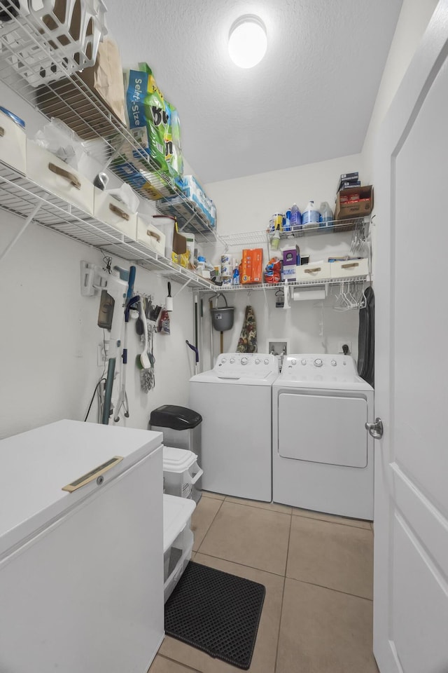 clothes washing area with washing machine and clothes dryer, a textured ceiling, and light tile patterned floors