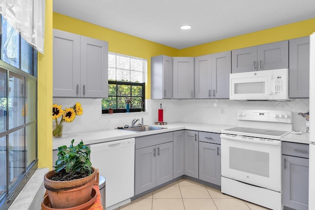 kitchen with sink, gray cabinetry, light tile patterned floors, white appliances, and backsplash