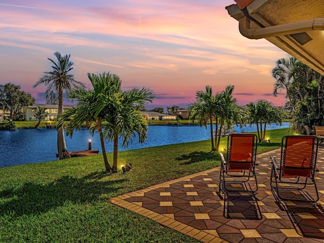 patio terrace at dusk featuring a water view and a lawn