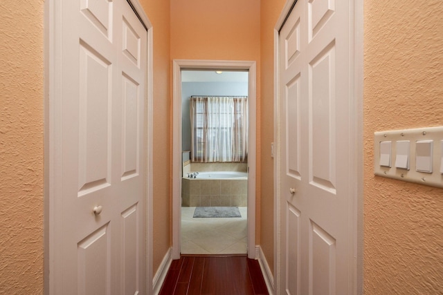 hallway featuring baseboards, dark wood finished floors, and a textured wall