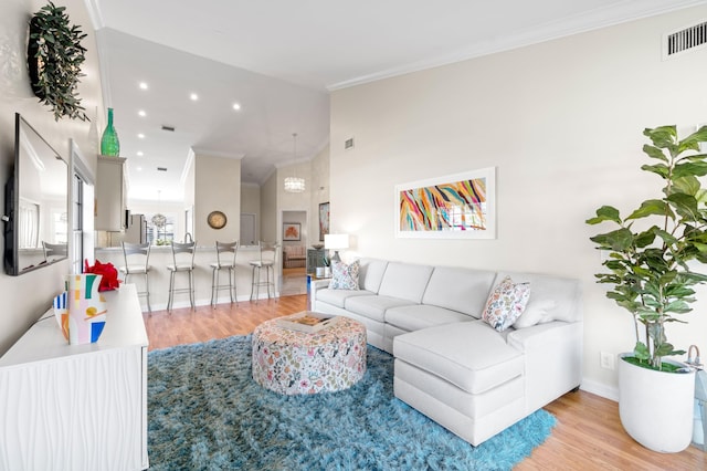 living room featuring vaulted ceiling, ornamental molding, and light hardwood / wood-style floors