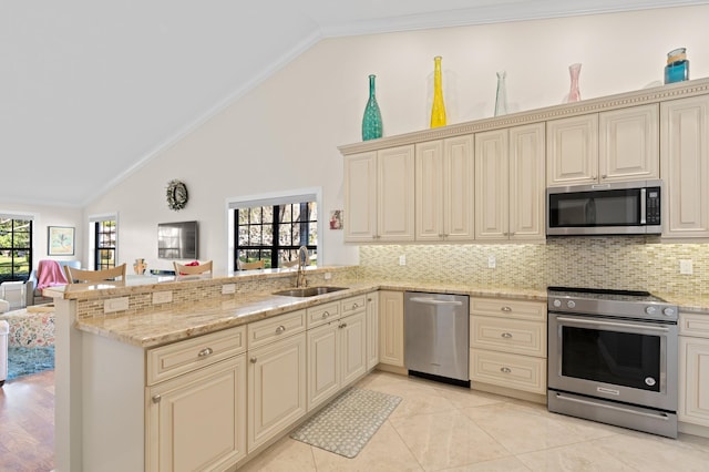 kitchen featuring appliances with stainless steel finishes, sink, kitchen peninsula, light stone countertops, and cream cabinetry