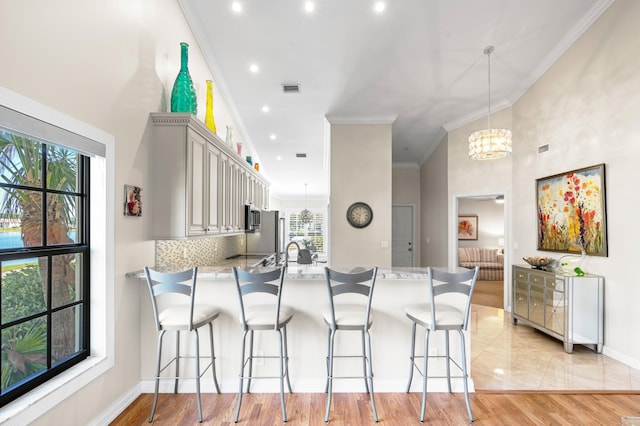 kitchen featuring hanging light fixtures, light hardwood / wood-style flooring, ornamental molding, kitchen peninsula, and decorative backsplash