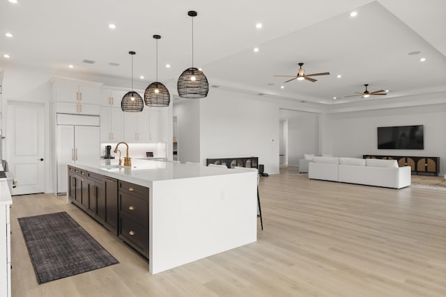 kitchen with decorative light fixtures, light countertops, open floor plan, white cabinetry, and a large island with sink