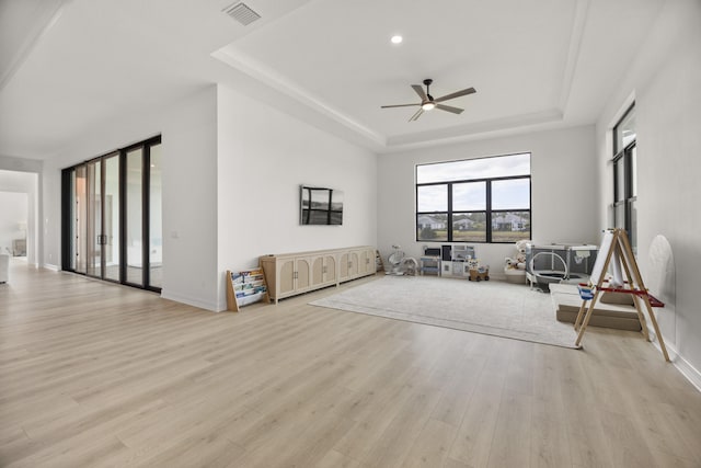 living room with light wood-style floors, ceiling fan, visible vents, and a raised ceiling