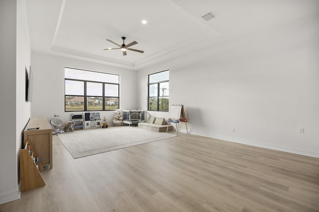 living room featuring light wood-style flooring, visible vents, a ceiling fan, baseboards, and a tray ceiling