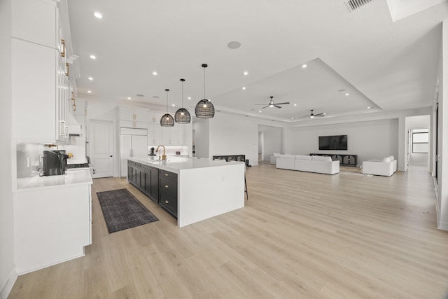 kitchen featuring open floor plan, white cabinets, a center island with sink, and hanging light fixtures