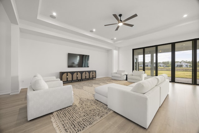 living room with recessed lighting, a raised ceiling, and light wood-style flooring