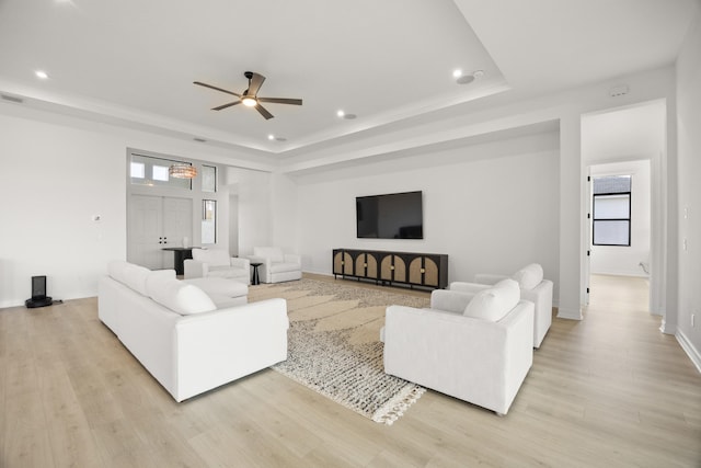 living room with light wood finished floors, baseboards, a raised ceiling, and recessed lighting