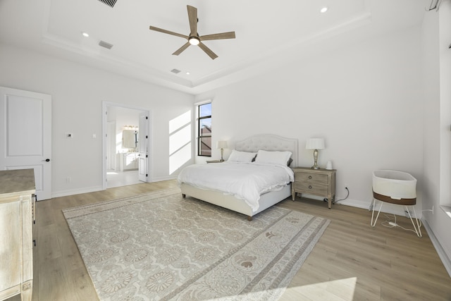 bedroom featuring light wood-style floors, a raised ceiling, visible vents, and baseboards